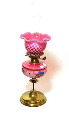 Lot 166 - ^ A late Victorian brass oil lamp, with pink floral glass reservoir and pink glass shade,...