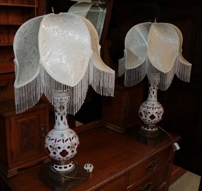 Lot 334 - ^ A pair of late 19th century pink and white overlay glass table lamps with gilt metal bases,...