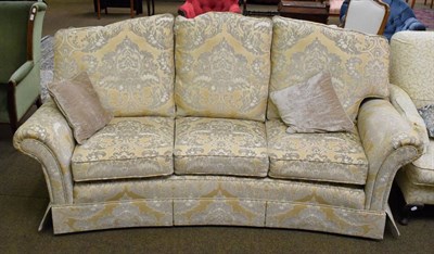 Lot 1357 - A three-seater sofa, modern, of curved form, upholstered in yellow and gold floral fabric, with six