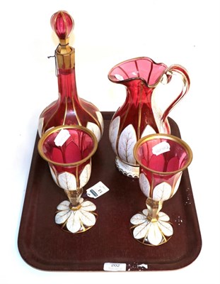 Lot 202 - A four piece cranberry and white glass overlay wine set comprising jug, decanter and pair of...