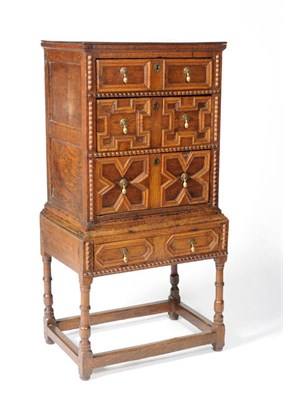 Lot 1491 - An Oak Chest on Stand, with three geometric and fielded panel drawers with brass split pin drop...