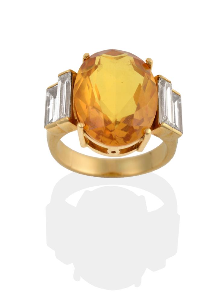 Lot 2035 - A Citrine and Diamond Ring, the oval cut citrine flanked by two graduated baguette cut diamonds...