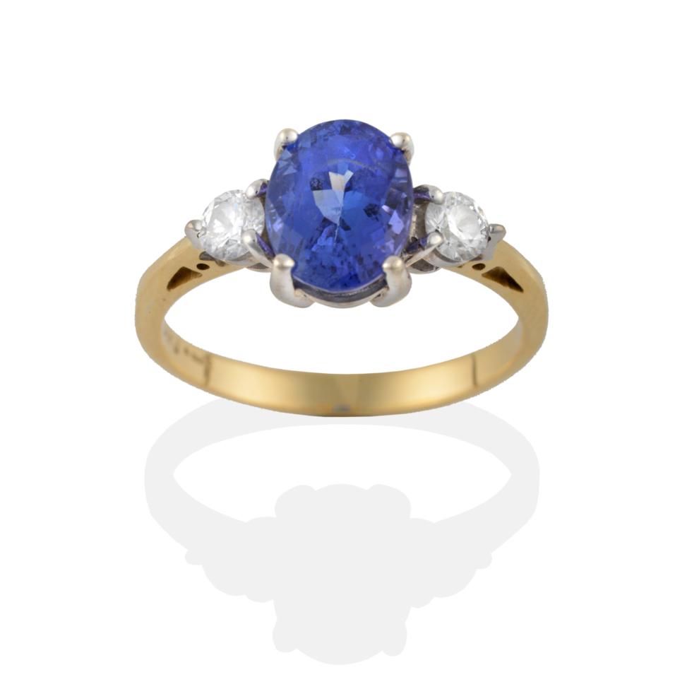 Lot 2089 - An 18 Carat Gold Tanzanite and Diamond Three Stone Ring, the oval cut tanzanite flanked by...