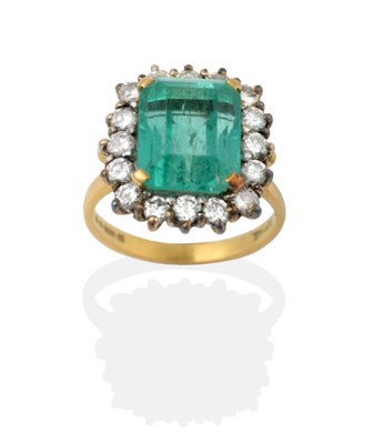 Lot 2152 - An 18 Carat Gold Emerald and Diamond Cluster Ring, the step-cut emerald in yellow claw...