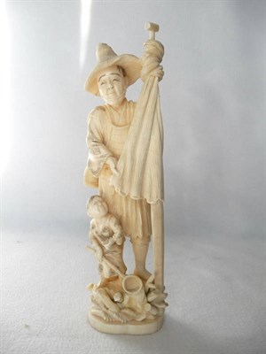 Lot 247 - A Japanese Ivory Okimono, circa 1930, as a man in a straw hat holding a net on a pole, a basket...