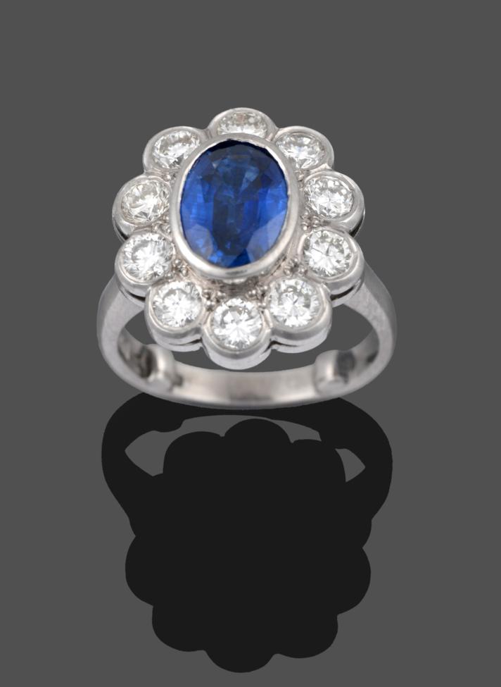 Lot 222 - A Platinum Sapphire and Diamond Cluster Ring, the oval mixed cut sapphire in a rubbed over...