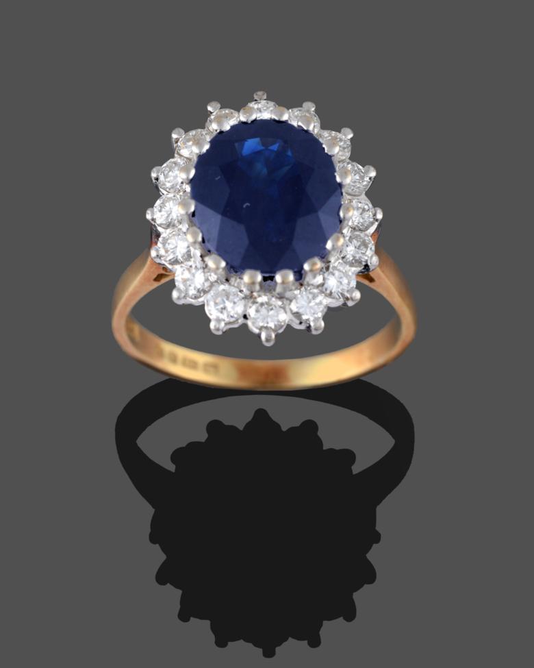 Lot 224 - An 18 Carat Gold Sapphire and Diamond Cluster Ring, the oval mixed cut sapphire within a border...