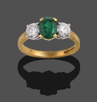 Lot 311 - An 18 Carat Gold Emerald and Diamond Three Stone Ring, the oval cut emerald between two round...