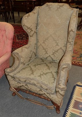 Lot 1334 - A wing back chair in the George III style, covered in worn green floral fabric, 84cm wide