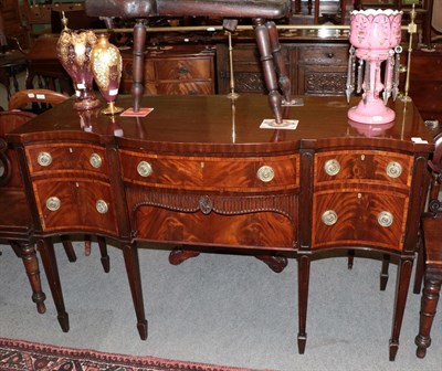 Lot 1343 - A late George III mahogany and tulipwood banded serpentine shaped sideboard, of attractive...