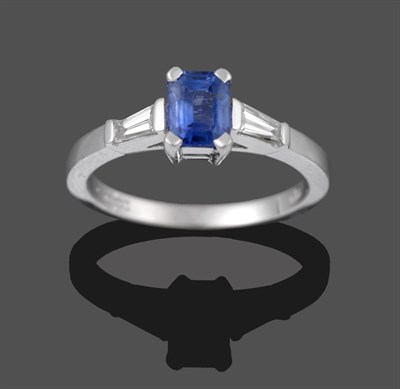 Lot 2024 - An 18 Carat White Gold Sapphire and Diamond Three Stone Ring, the emerald-cut sapphire in a...