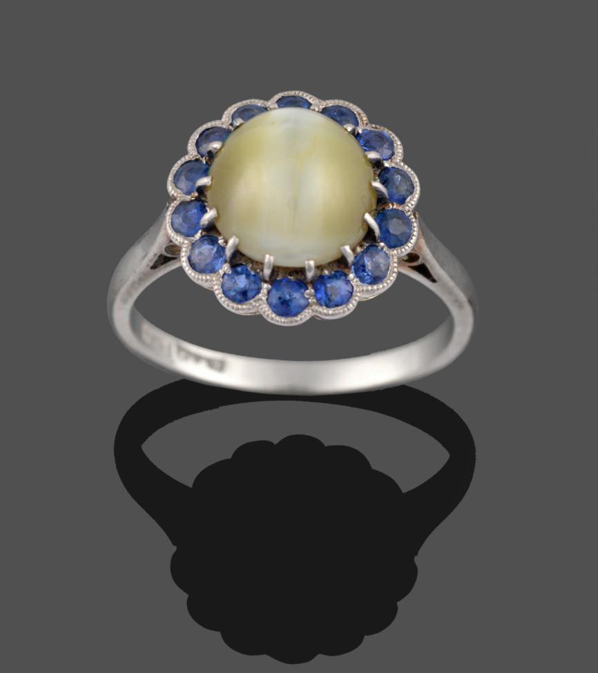 Lot 2118 - A Cats-Eye Chrysoberyl and Sapphire Cluster Ring, the circular cabochon cats-eye chrysoberyl in...