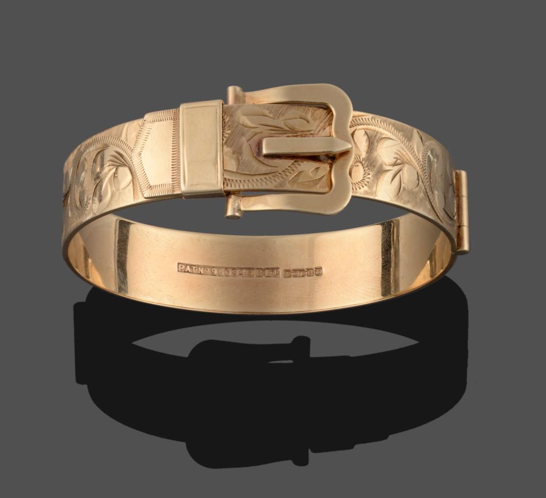 Lot 2176 - A 9 Carat Gold Hinged Bangle, by Bracelon Ltd, in the form of a belt buckle with floral motif...