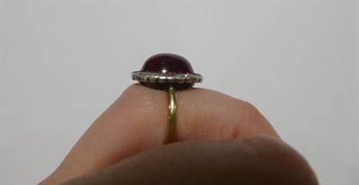 Lot 2191 - A Synthetic Ruby and Diamond Cluster Ring, the oval cabochon synthetic ruby within a border of...