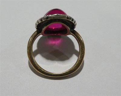 Lot 2191 - A Synthetic Ruby and Diamond Cluster Ring, the oval cabochon synthetic ruby within a border of...