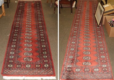 Lot 458 - A pair of narrow Lahore Bokhara runners, each with a terracotta field of guls, enclosed by...