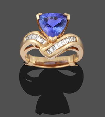 Lot 3293 - A Tanzanite and Diamond Ring, a trilliant cut tanzanite in yellow claw settings, to baguette...
