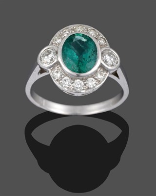 Lot 3307 - An Emerald and Diamond Ring, the oval cut emerald within a border of round brilliant cut...