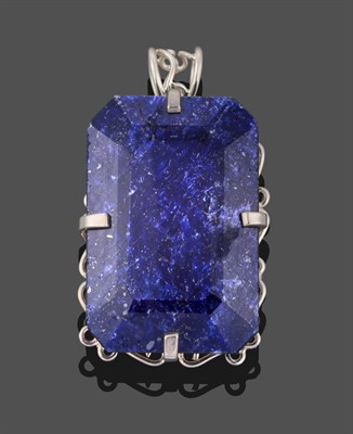 Lot 3311 - A Sapphire Pendant, the emerald-cut sapphire in a white claw setting to a scroll border,...