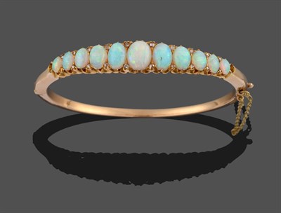 Lot 3329 - An Opal and Diamond Bangle, eleven graduated oval cabochon opals with pairs of rose cut diamond...