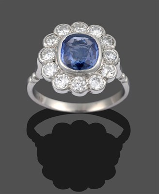 Lot 3353 - A Sapphire and Diamond Cluster Ring, the cushion cut sapphire within a border of round...