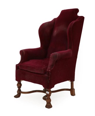 Lot 352 - A 17th Century Style Wing-Back Chair, covered in worn red velvet, with rounded arm supports and...