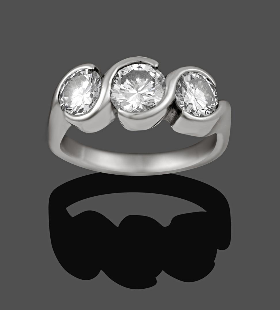 Lot 1003 - A Diamond Three Stone Ring, the graduated round brilliant cut diamonds in swirl tension...