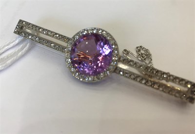 Lot 1045 - A Diamond and Pinkish-Purple Stone Bar Brooch, the round cut pinkish-purple stone within a...