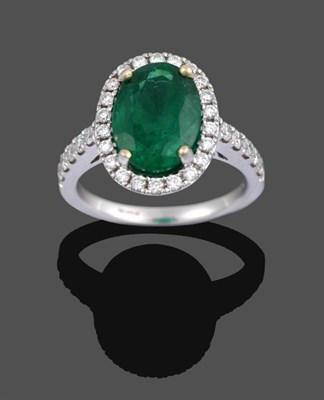 Lot 1048 - An 18 Carat Gold Emerald and Diamond Cluster Ring, the oval cut emerald in a yellow four claw...