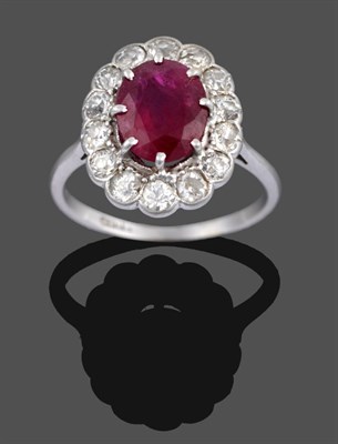 Lot 1050 - A Ruby and Diamond Cluster Ring, the oval cut ruby in a white claw setting within a border of...