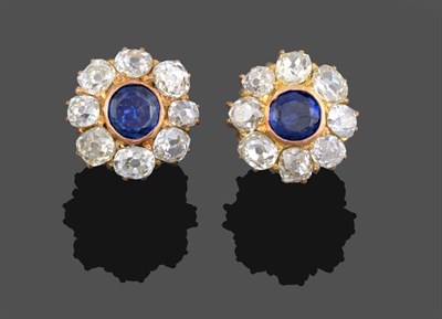 Lot 1077 - A Pair of Sapphire and Diamond Cluster Earrings, the round cut sapphire in a yellow rubbed over...