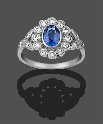 Lot 1128 - A Sapphire and Diamond Cluster Ring, the oval cut sapphire within a border of round brilliant...