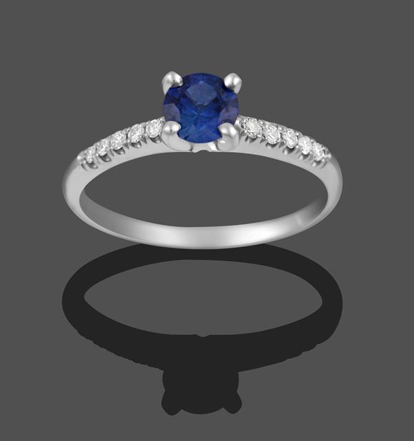 Lot 2009 - A 14 Carat White Gold Sapphire and Diamond Ring, the round cut sapphire in a four claw setting,...