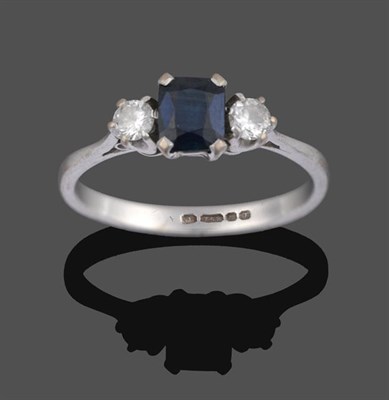 Lot 2010 - An 18 Carat White Gold Sapphire and Diamond Three Stone Ring, the emerald-cut sapphire sits between