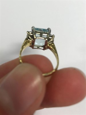 Lot 2029 - An Aquamarine and Diamond Ring, the emerald-cut aquamarine sits between trios of round...