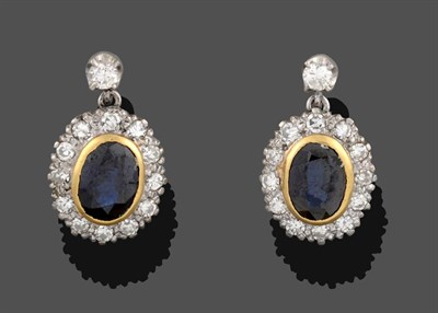 Lot 2137 - A Pair of Sapphire and Diamond Drop Earrings, the oval cut sapphire in a yellow rubbed over...