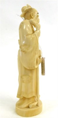 Lot 135 - A Japanese Ivory Okimono of a Sage, Meiji period, standing in flowing robes holding a peach and...