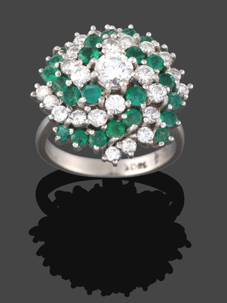 Lot 239 - An Emerald and Diamond Cluster Ring, a round brilliant cut diamond within a swirling border of...