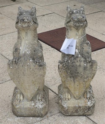 Lot 1114 - A pair of weathered composition seated dogs bearing shields