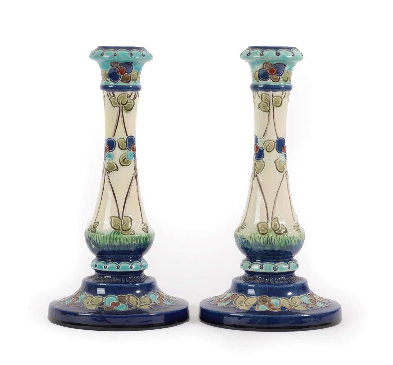 Lot 2004 - A Pair of Burmantofts Faience Pottery Candlesticks, decorated with flower heads in blues and...