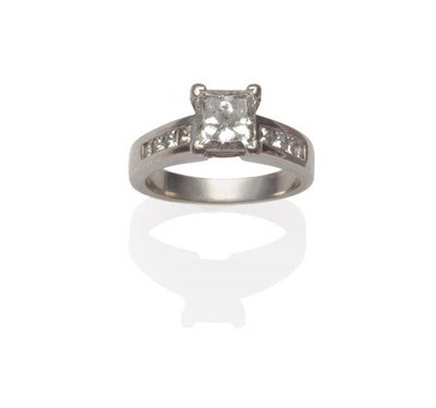 Lot 565 - A Princess Cut Diamond Solitaire Ring, in a white claw setting with a row of princess cut...