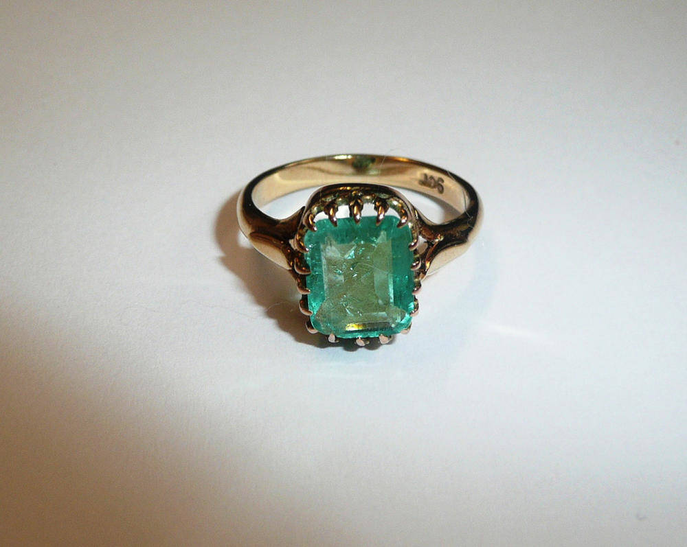 Lot 701 - An Emerald Ring, the emerald-cut stone in a yellow claw setting, to fleur-de-lys design...