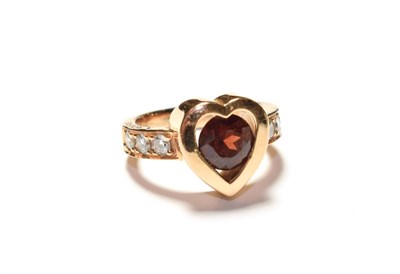 Lot 192 - An heart shaped ring, with a red synthetic stone centrally and diamond set shoulders, stamped...