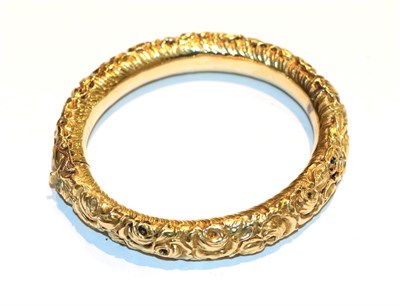 Lot 82 - A floral chased hinged bangle, inner measurements 5.8cm by 6.6cm