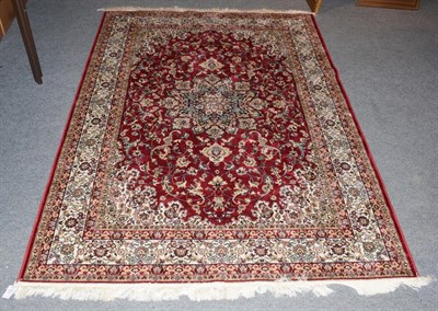 Lot 1271 - A machine made rug of Oriental design, the blood red floral field centred by medallion framed...