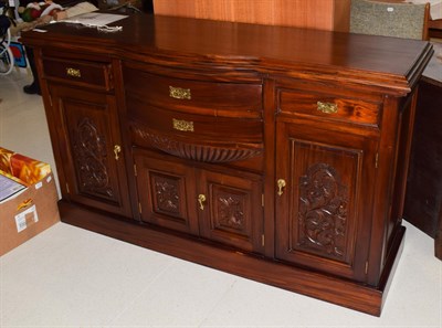 Lot 1403 - A reproduction bow-fronted sideboard with stained finish and carved panels, 157cm by 54cm by 94cm