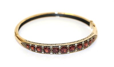 Lot 35 - A 9 carat gold garnet and diamond hinged bangle, the eleven graduated garnets with eight-cut...