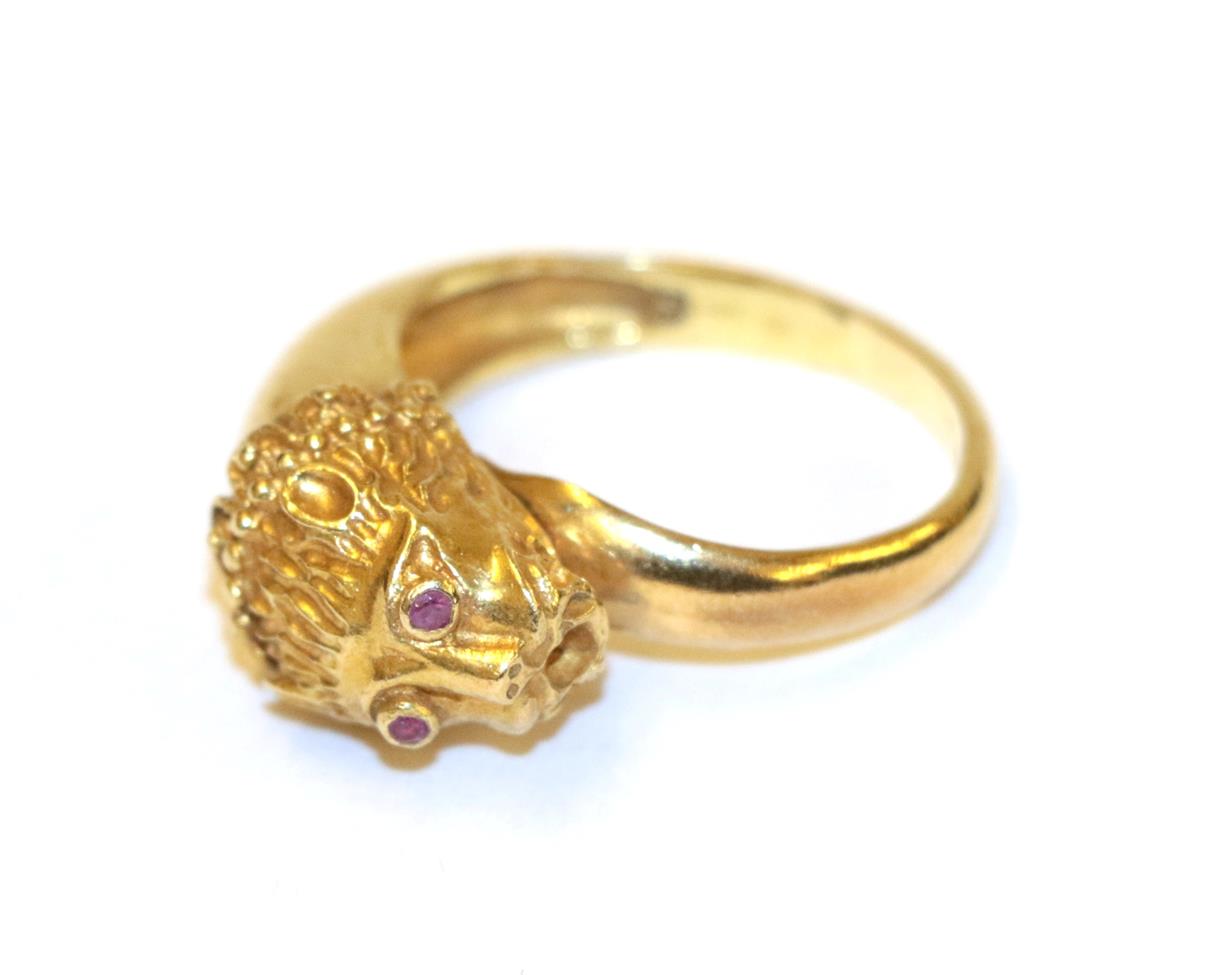 Lot 75 - A lion mask ring, the lion mask motif with round cut ruby eyes in yellow collet settings, to a...