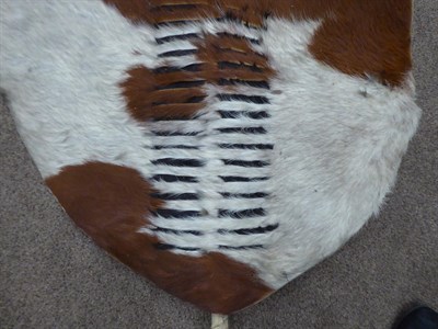 Lot 328 - Two 20th Century Zulu Cow Hide Shields, each of tan and white colouring, of elliptical form,...