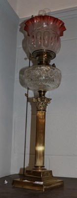 Lot 471 - A Victorian brass Corinthian columnar oil lamp with clear glass reservoir and cranberry shade